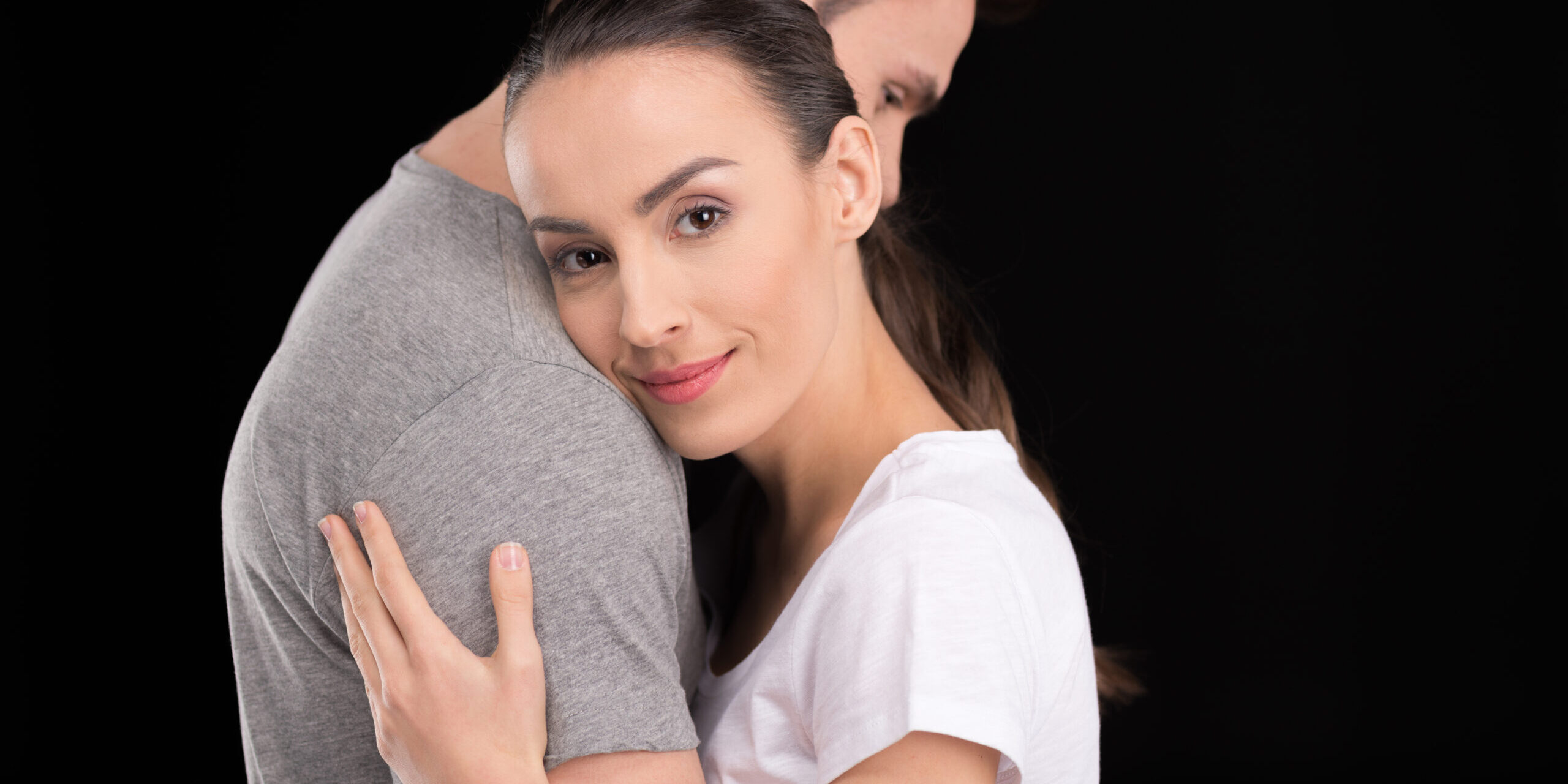portrait of smiling woman bonding to man and looking to camera isolated on black